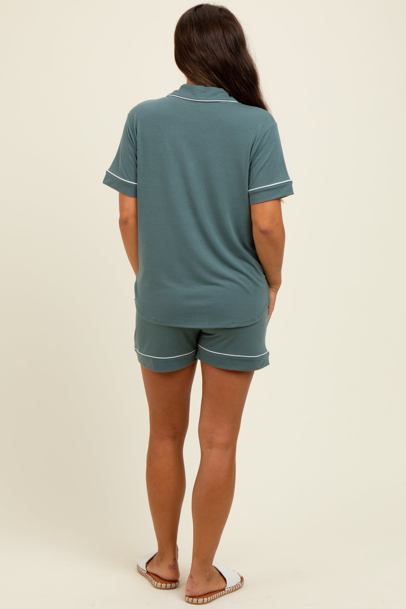 woman wearing a green maternity pajama set with shorts and a short-sleeve top, seen from the back