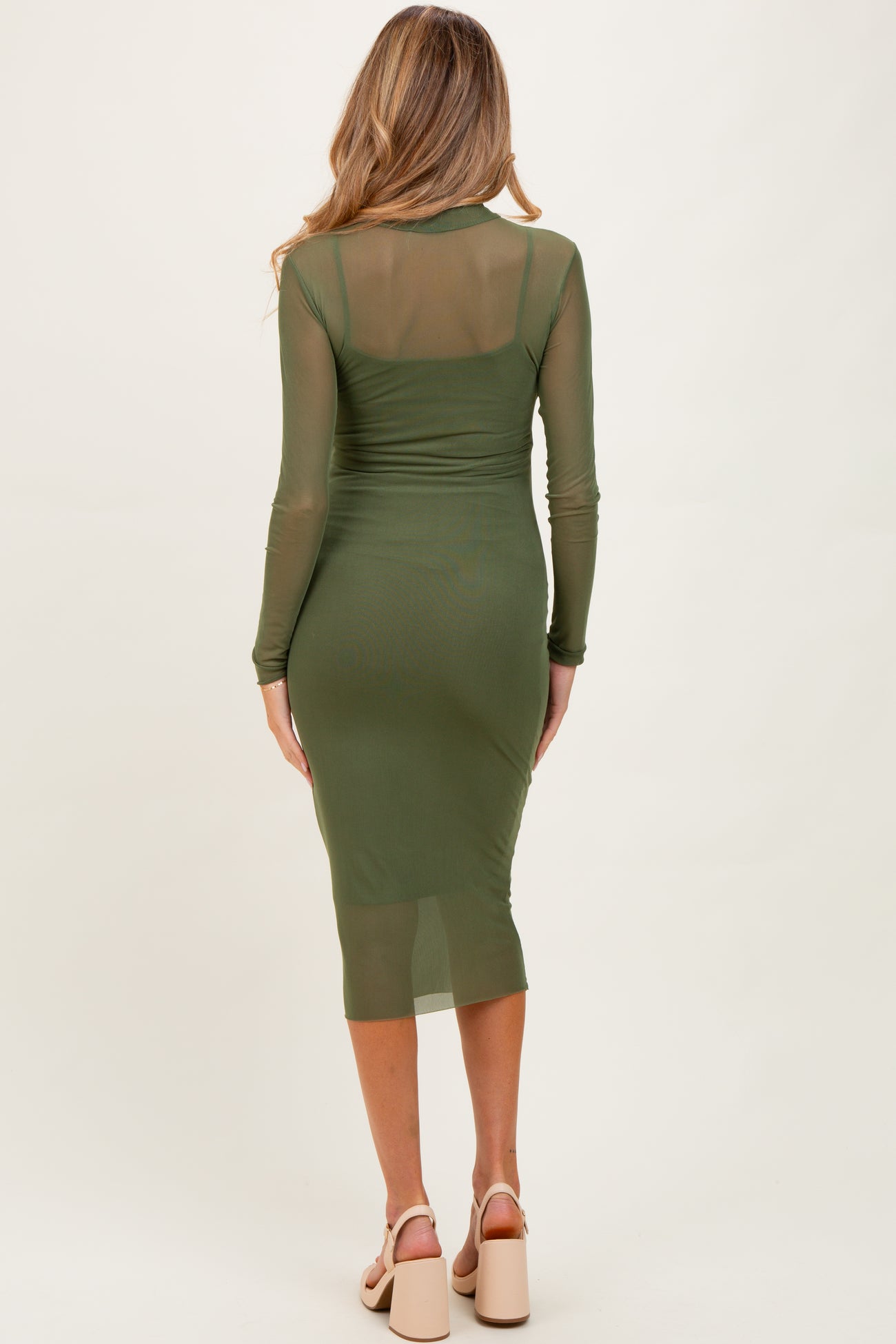 woman wearing an olive green long sleeve maternity dress with a form-fitting silhouette and midi length, showing her baby bump