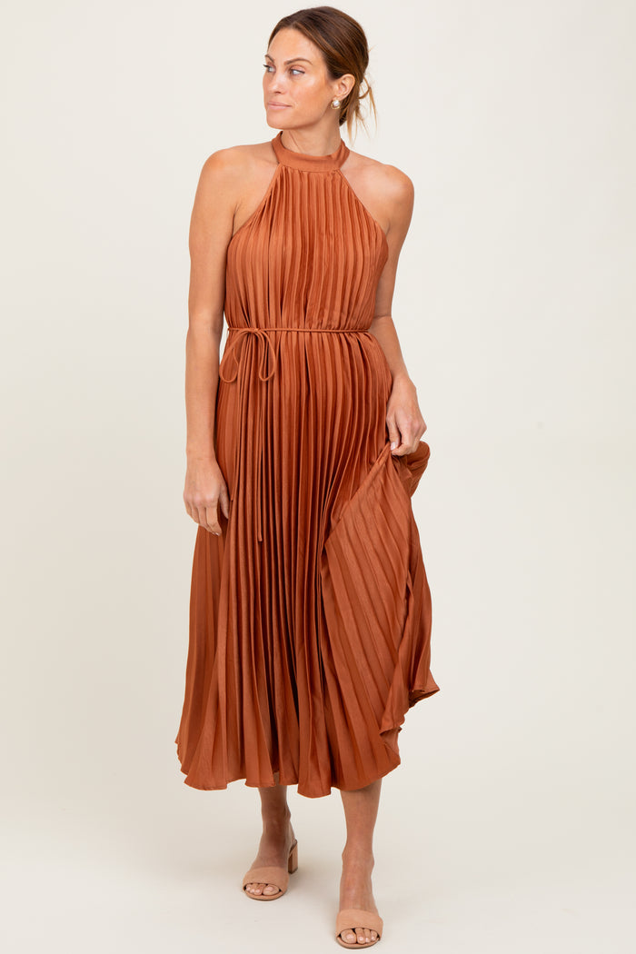woman wearing a rust-colored pleated midi dress with a halter neck and tie waist detail