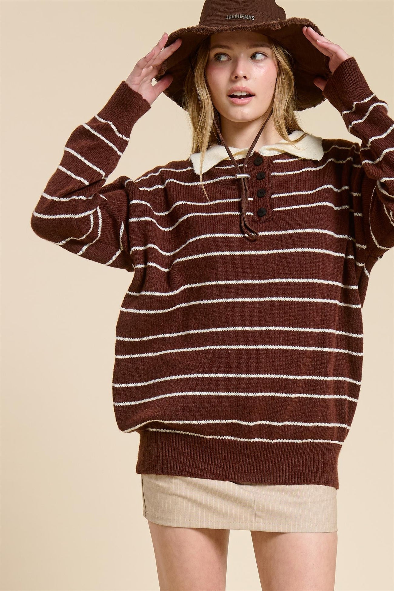 woman wearing a brown striped oversized sweater with a white collar and a beige mini skirt, paired with a brown hat