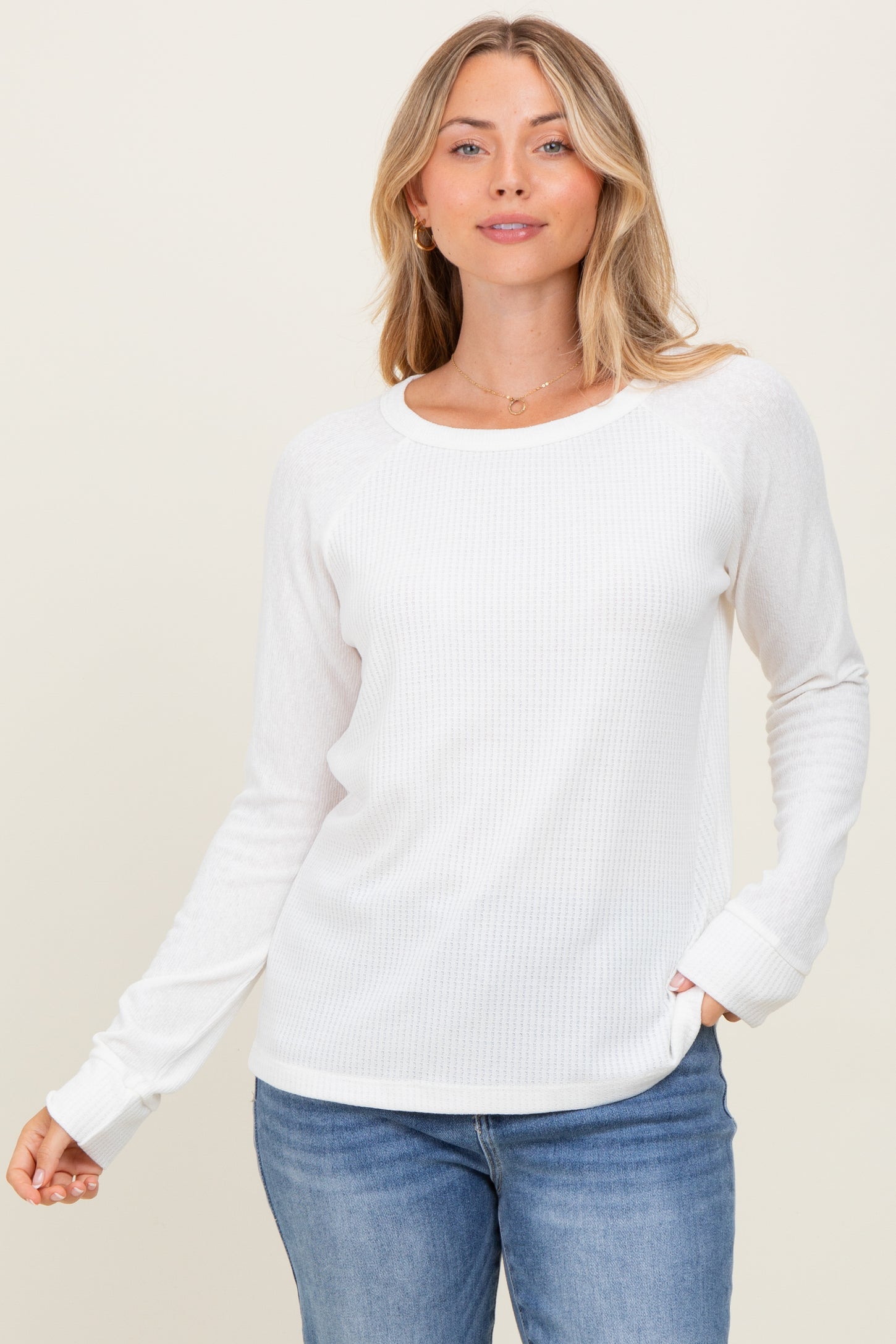 woman wearing a white long sleeve textured top with a round neckline and relaxed fit, paired with blue jeans
