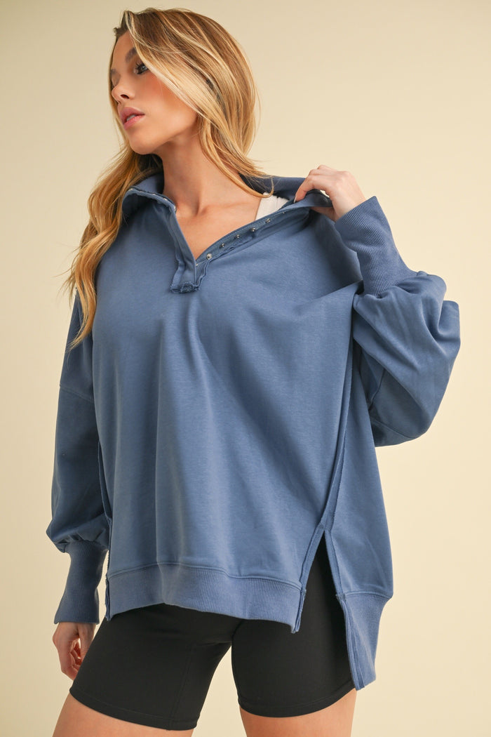 woman wearing a blue oversized pullover sweatshirt with a collar and side slits, paired with black bike shorts