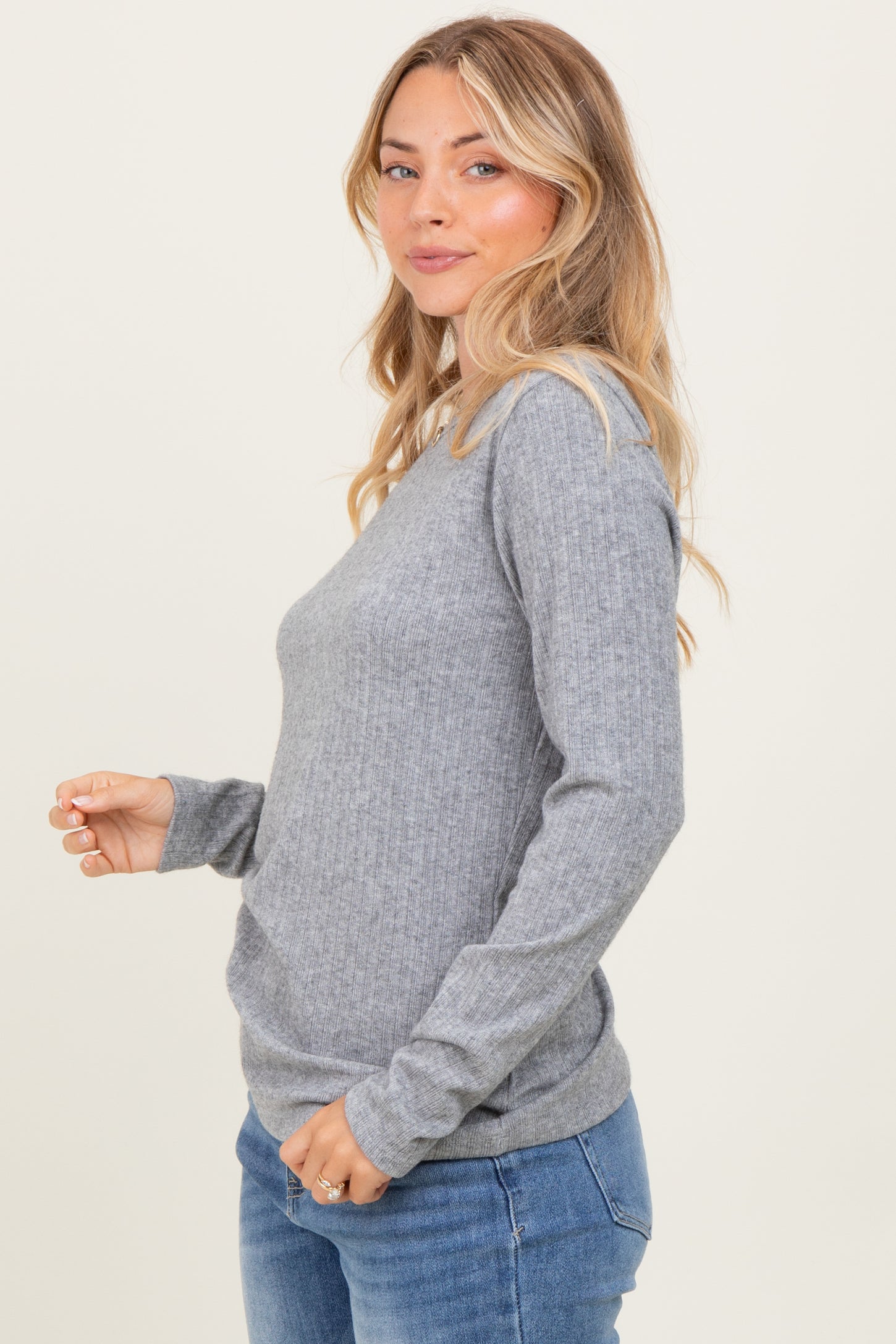 woman wearing a gray ribbed long sleeve top and blue jeans, smiling and facing sideways