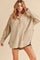 woman wearing a beige oversized fleece pullover with a buttoned neckline and front pockets, styled with distressed shorts
