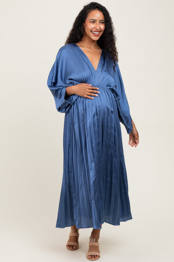 woman wearing a blue pleated maternity dress with a deep v-neck and a cinched waist, holding her baby bump