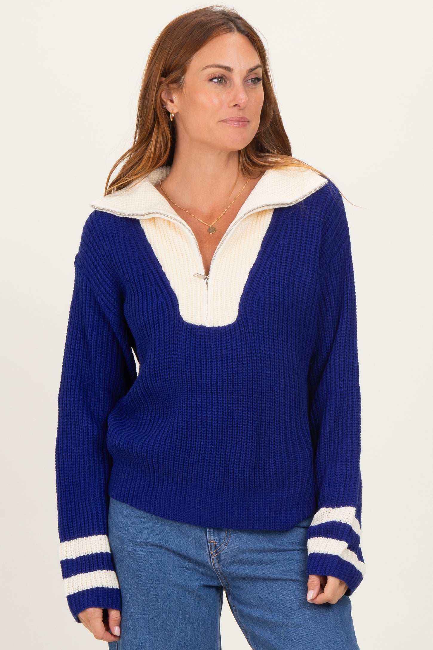 woman wearing a blue and cream color block oversized sweater with a half zip collar and stripe details on the sleeves