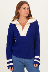 woman wearing a blue and cream color block oversized sweater with a half zip collar and stripe details on the sleeves
