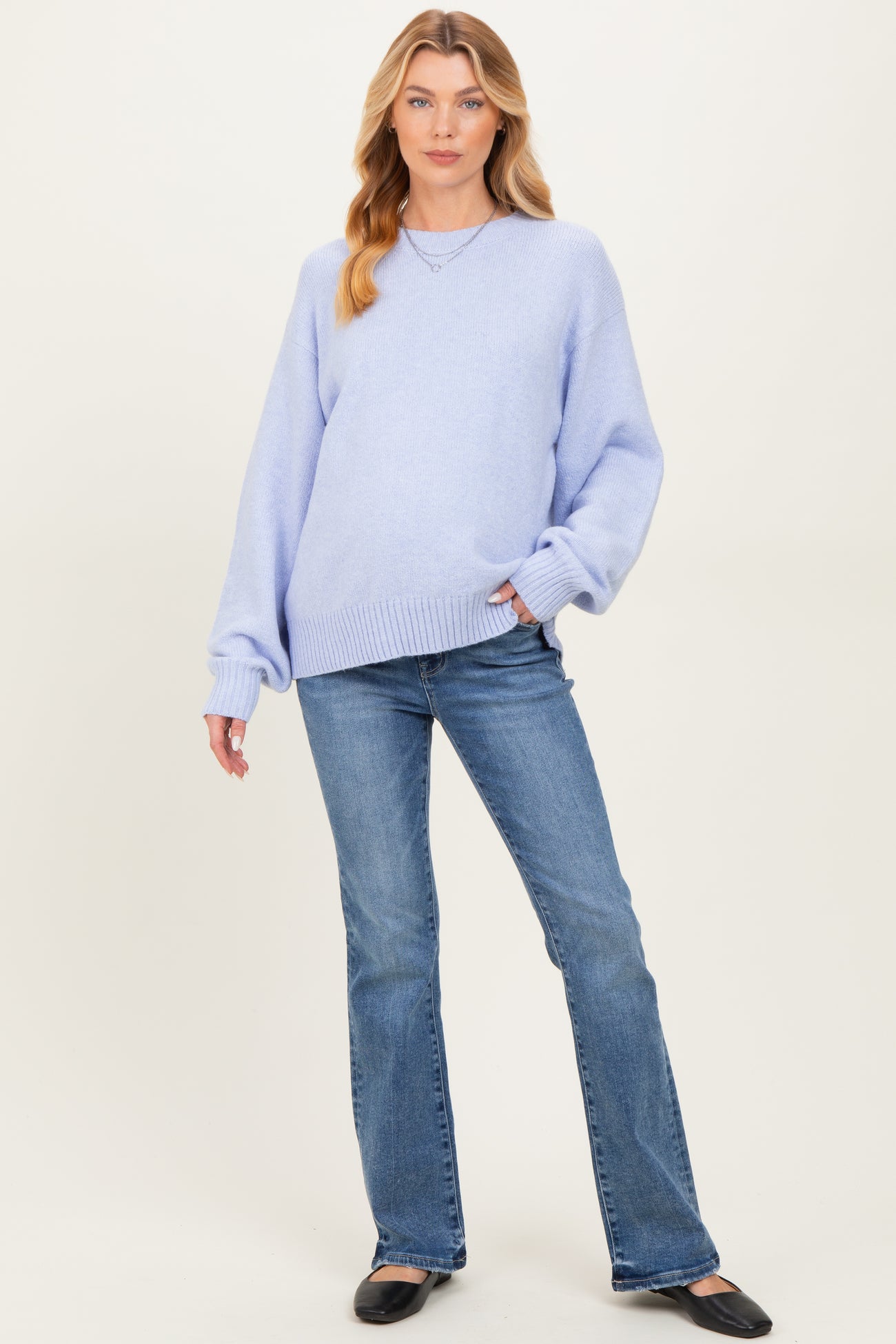 woman wearing a light purple oversized maternity sweater with long sleeves and blue flared jeans