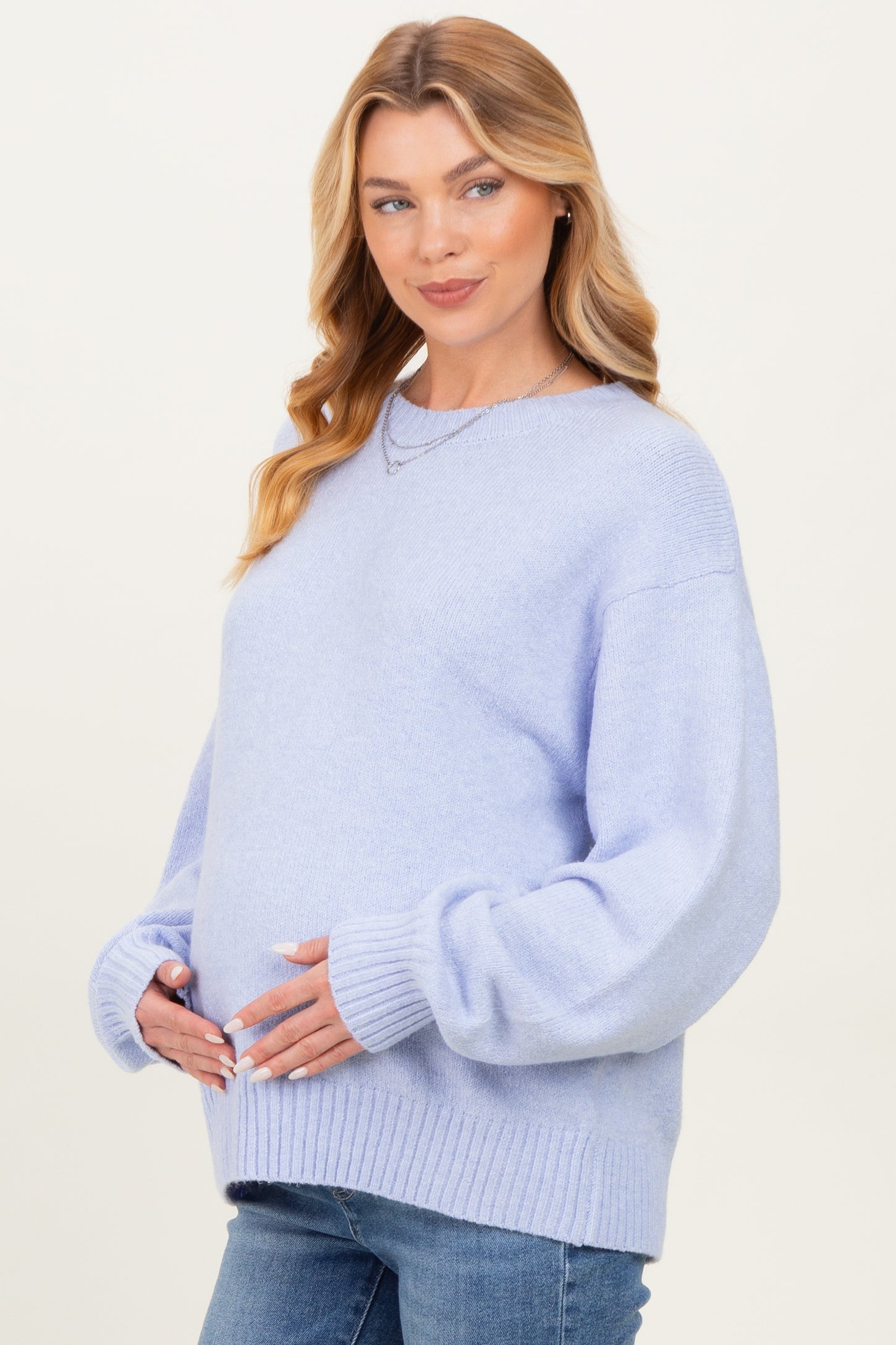 woman wearing a light blue maternity sweater with balloon sleeves and holding her baby bump