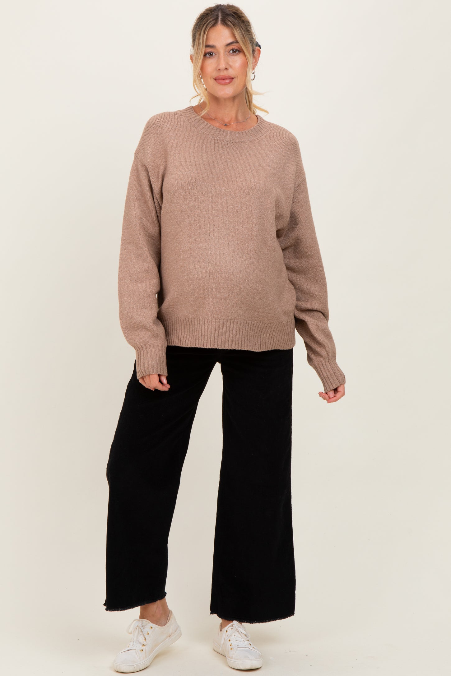woman wearing a beige maternity sweater with long sleeves and black wide-leg pants, showing a baby bump