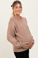 woman wearing a tan oversized maternity sweater and holding her baby bump