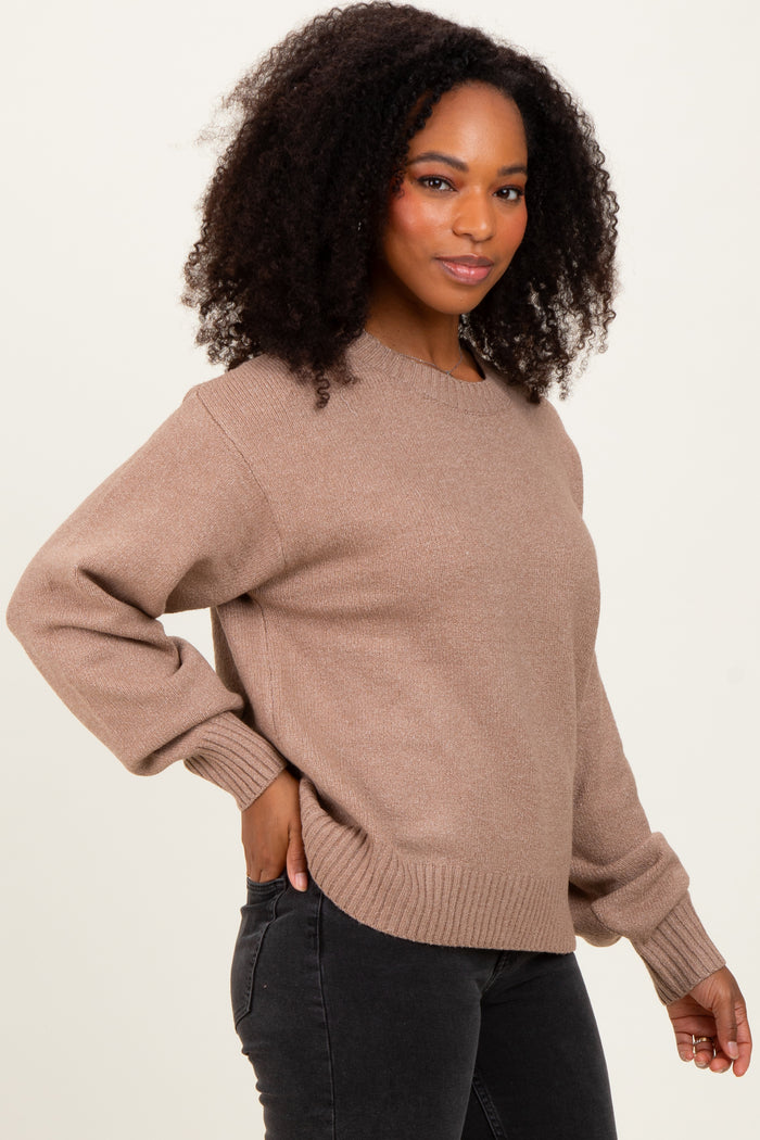woman wearing a taupe oversized sweater with ribbed hem and cuffs, standing against a plain background