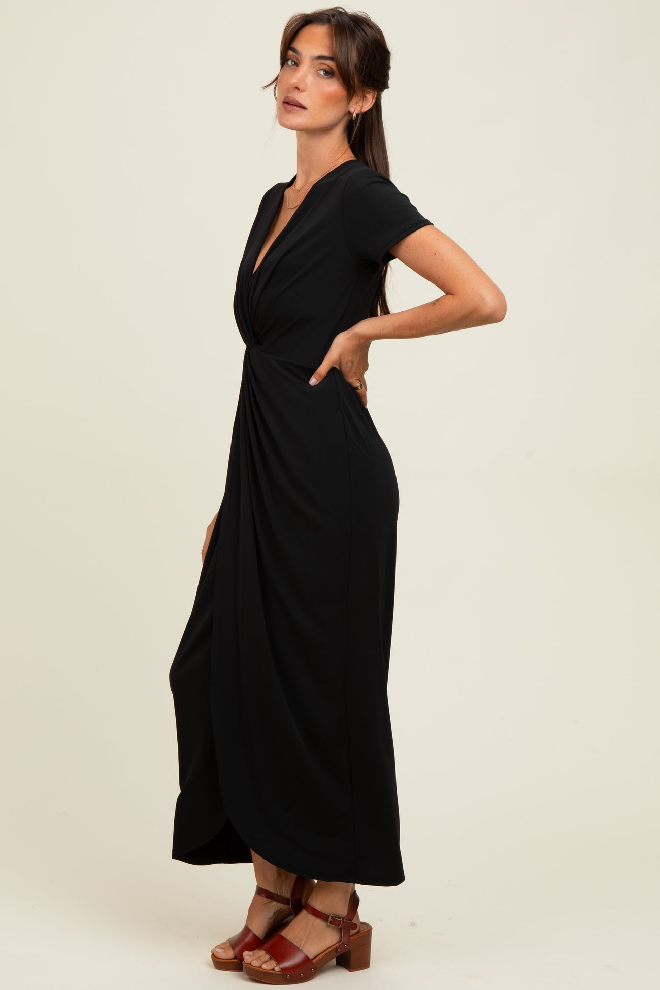woman wearing a black short sleeve maxi dress with a twisted front detail and red heeled sandals