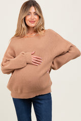 woman wearing a brown oversized ribbed maternity sweater and holding her baby bump