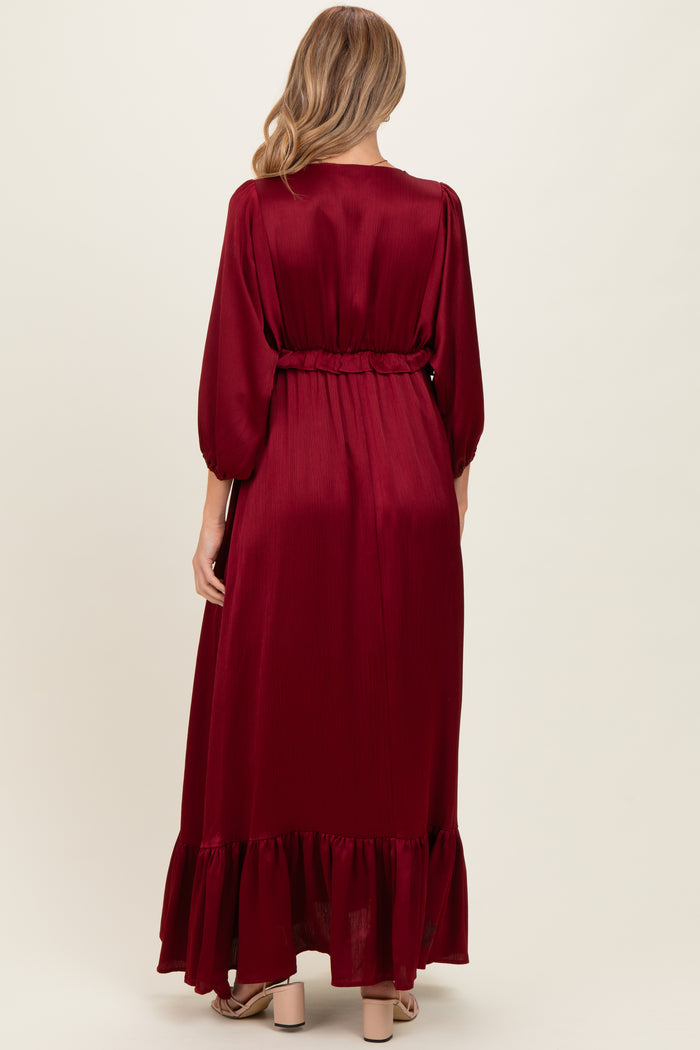 woman wearing a burgundy long sleeve maternity dress with a ruffled hem and belted waist, showing her baby bump