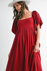 woman wearing a red puff sleeve maxi dress with a square neckline and pleated detailing