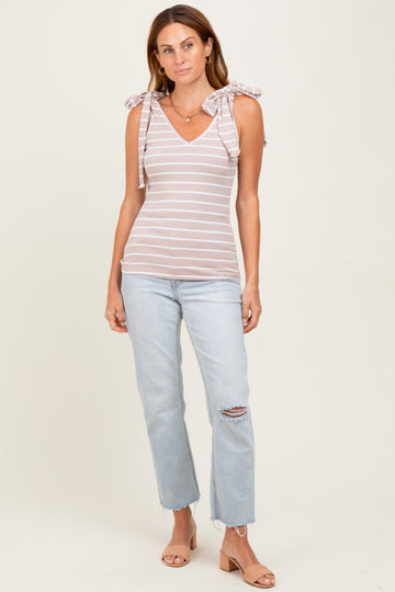 woman wearing a light pink and white striped tank top with bow tie straps and paired with distressed light blue jeans