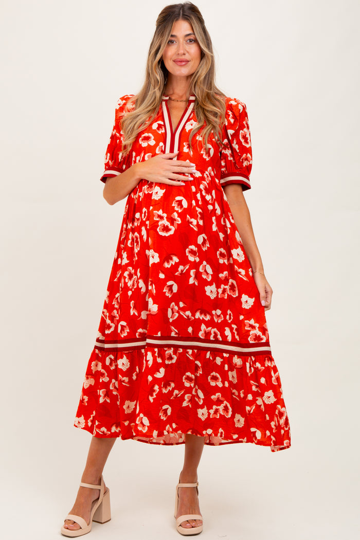 woman wearing a red floral maternity dress with puffed sleeves and tiered skirt, holding her baby bump