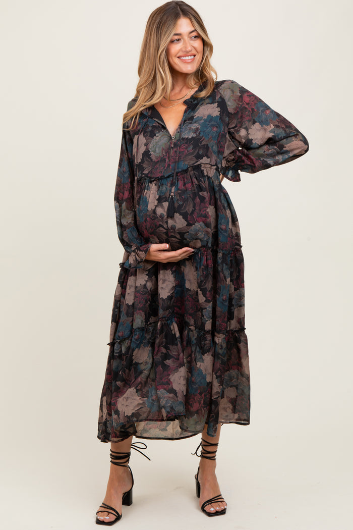woman wearing a flowy dark floral maternity dress with long sleeves and tiered design, holding her baby bump
