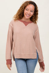 woman wearing a beige oversized waffle knit sweater with a maroon collar and side slits, paired with blue jeans