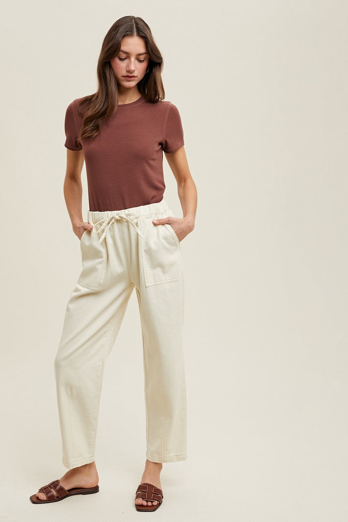 woman wearing a brown ribbed short sleeve top and cream drawstring pants with side pockets