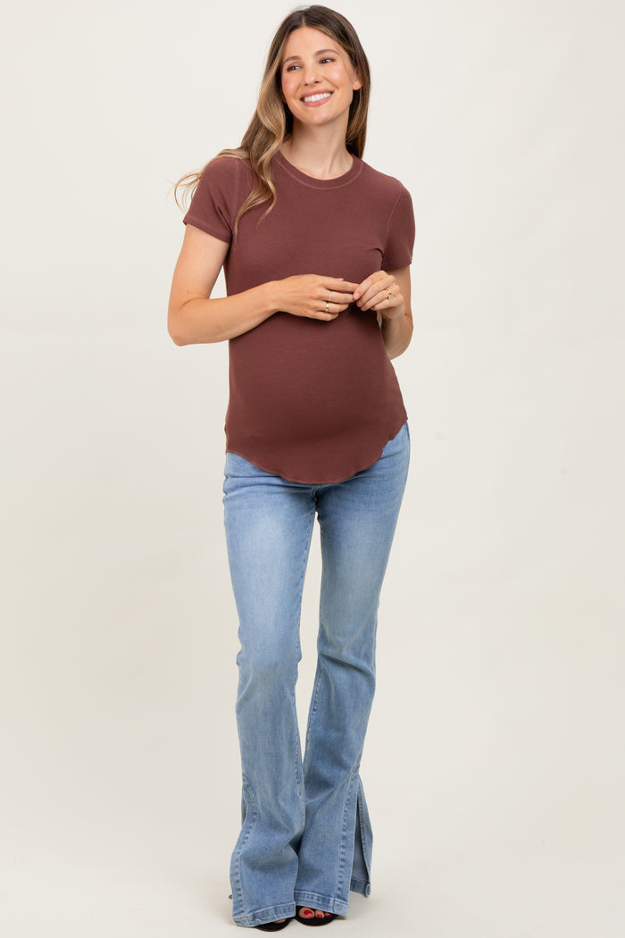 woman wearing a brown fitted maternity t-shirt and flared blue jeans, showcasing her baby bump