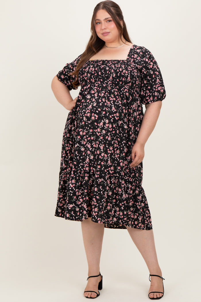 woman wearing a black floral maternity plus dress with puff sleeves and a tiered ruffle hem, showing her baby bump