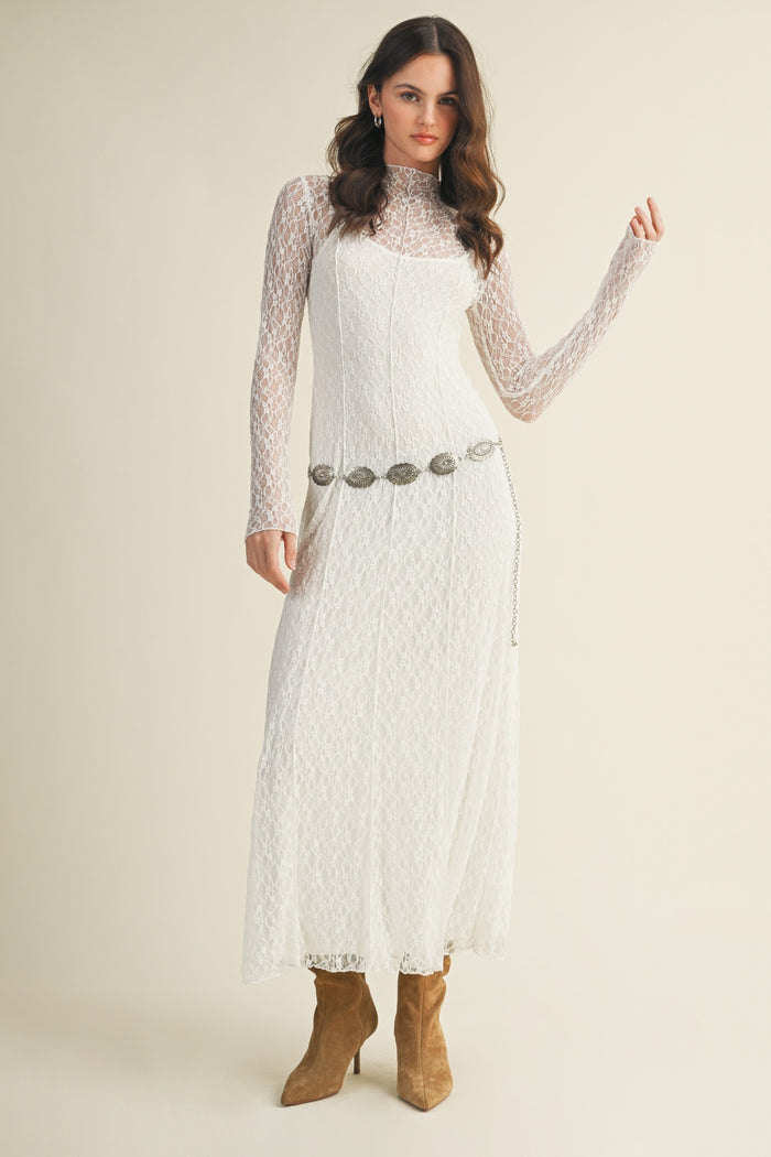 woman wearing a white lace long sleeve maxi dress with a silver belt and brown heeled boots