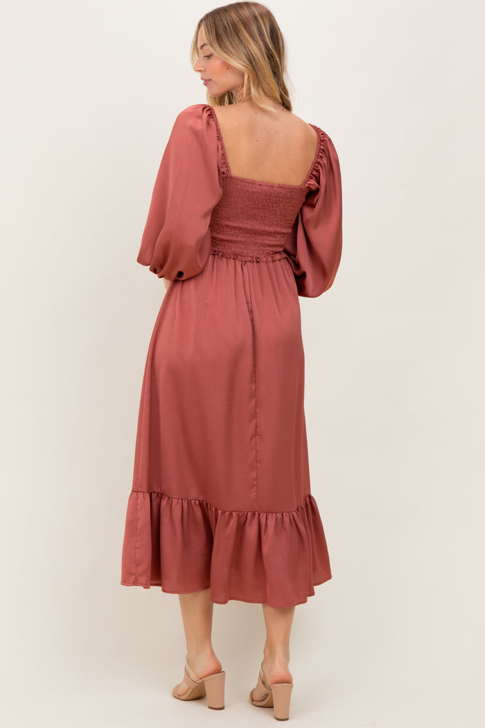woman wearing a rust-colored mid-length dress with puff sleeves and a smocked bodice, standing with her back to the camera