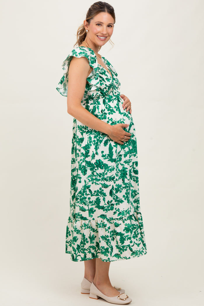 woman wearing a green and white floral maternity dress with ruffles, smiling and holding her baby bump