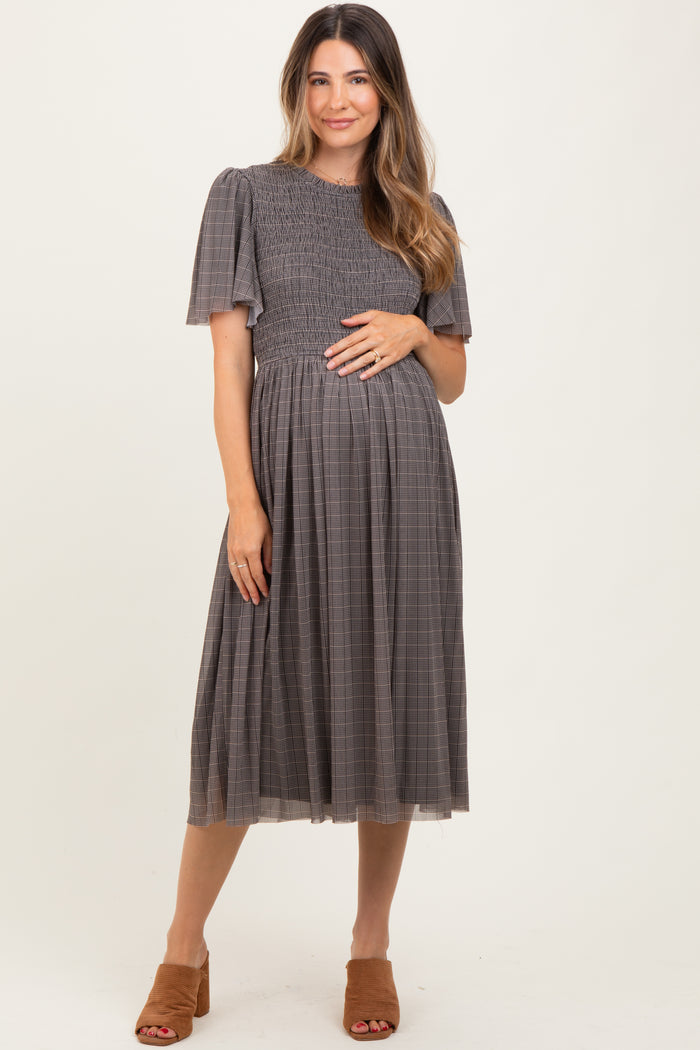 woman wearing a gray checkered maternity dress with short sleeves and a smocked bodice, holding her baby bump