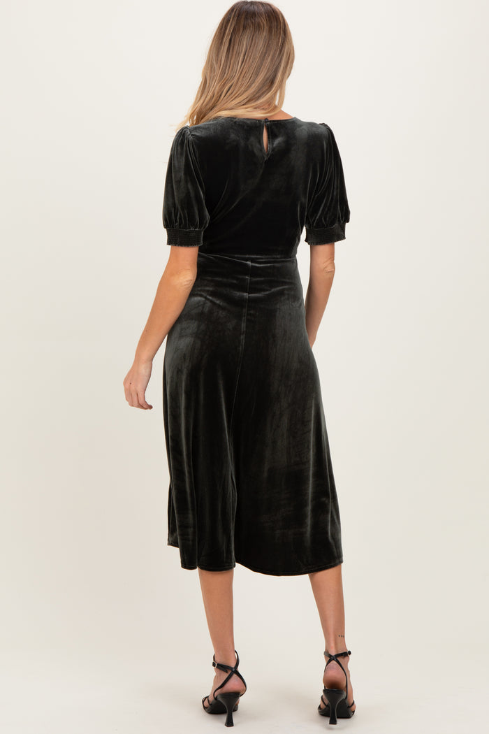 woman wearing a dark green velvet maternity dress with puff sleeves and a keyhole back detail, showing a baby bump