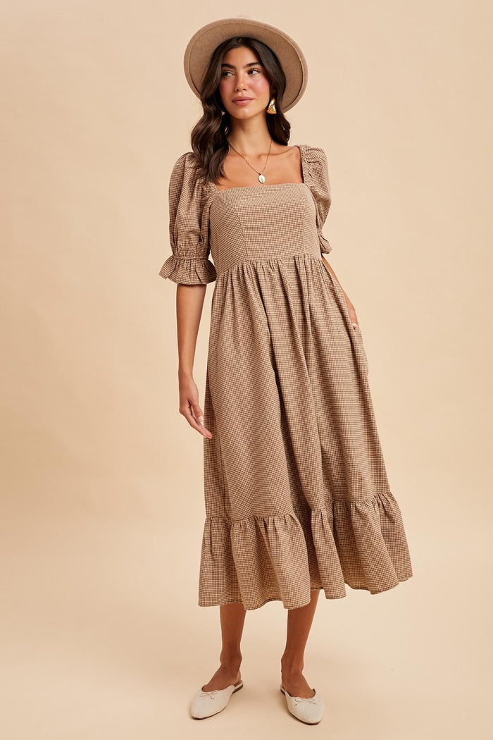 woman wearing a tan square neck midi dress with puff sleeves and ruffle hem, paired with a wide-brim hat and slip-on shoes