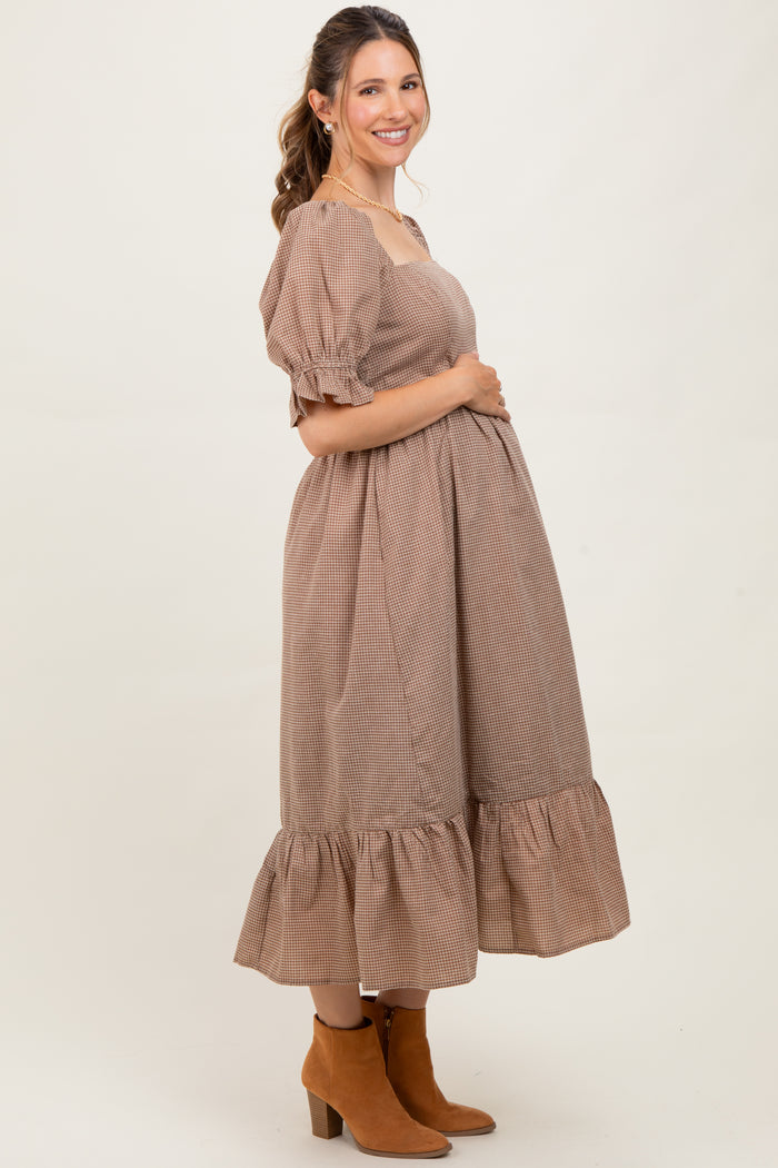 woman wearing a brown checkered maternity dress with puff sleeves and a ruffled hem, showing her baby bump