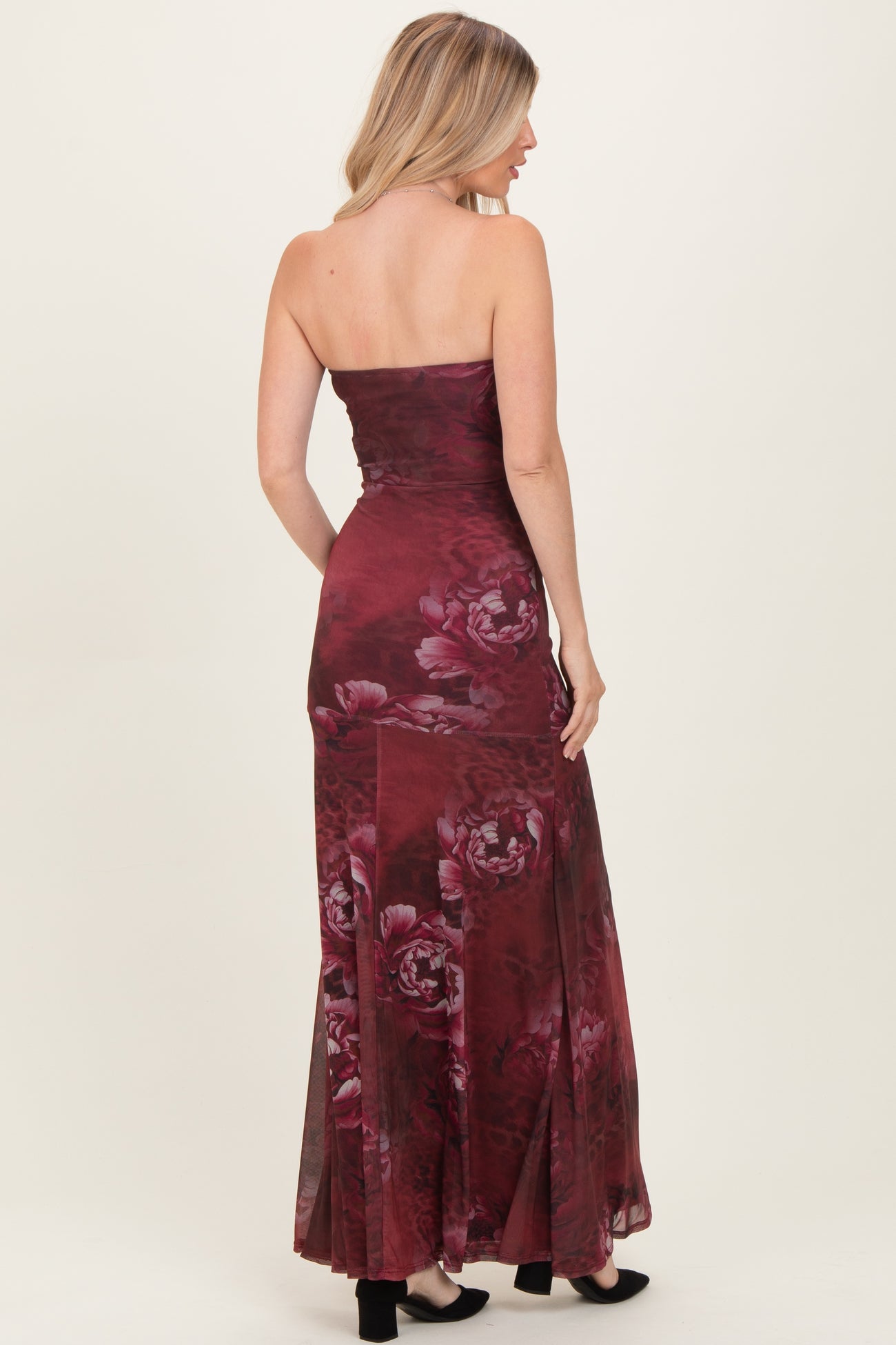 woman wearing a burgundy strapless floral maxi dress, showcasing a fitted bodice and flowing skirt from the back