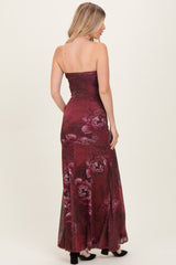 woman wearing a burgundy strapless floral maxi dress, showcasing a fitted bodice and flowing skirt from the back