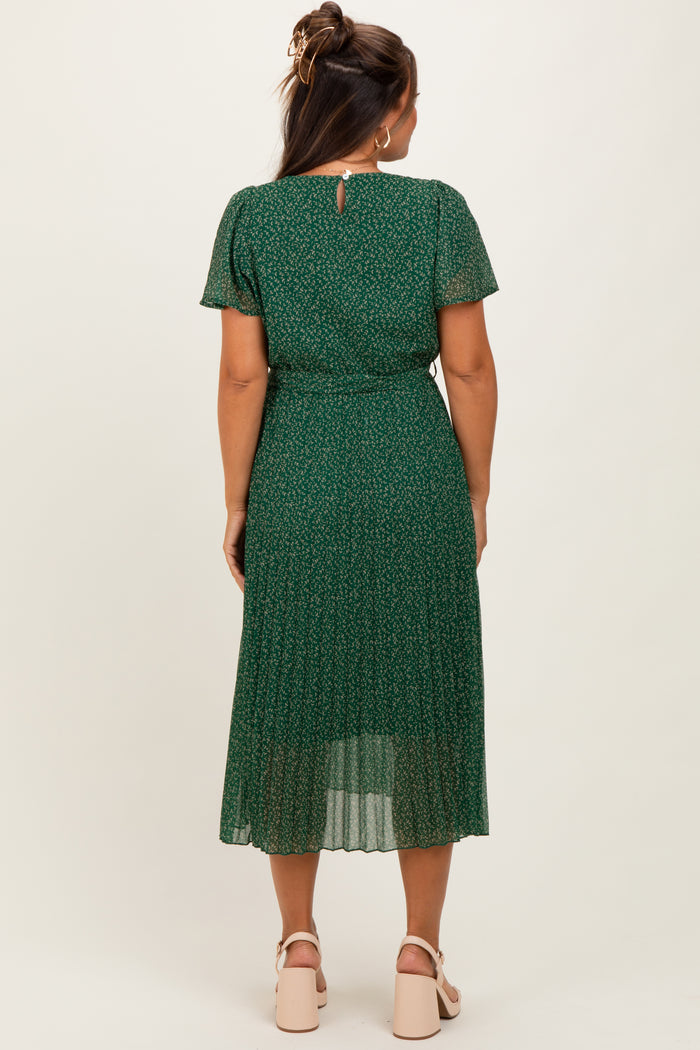 woman wearing a green maternity dress with a floral pattern and pleated skirt, showing her baby bump from the back