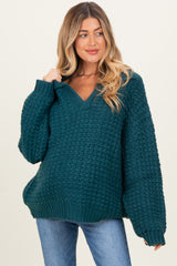woman wearing a dark teal oversized knitted maternity sweater with a v-neck and relaxed fit, showing a baby bump