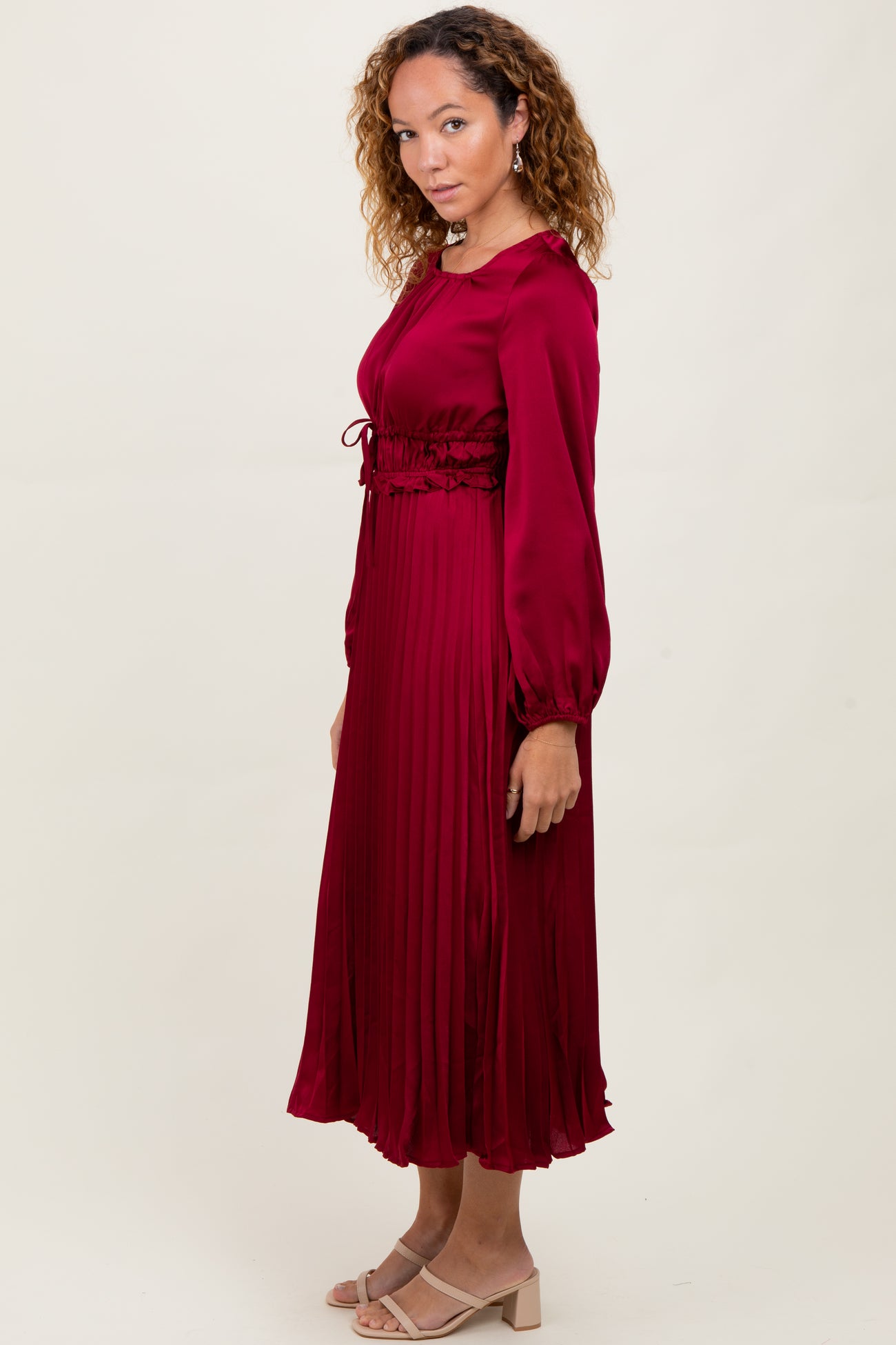 woman wearing a burgundy pleated long sleeve dress with a cinched waist and a flowy silhouette