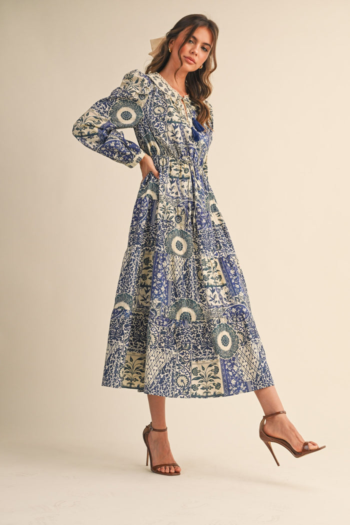 woman wearing a long sleeve blue and cream patterned maxi dress with a tiered design and a cinched waist