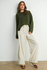 woman wearing an olive green oversized sweater and cream wide-leg pants with a subtle pattern and drawstring waist
