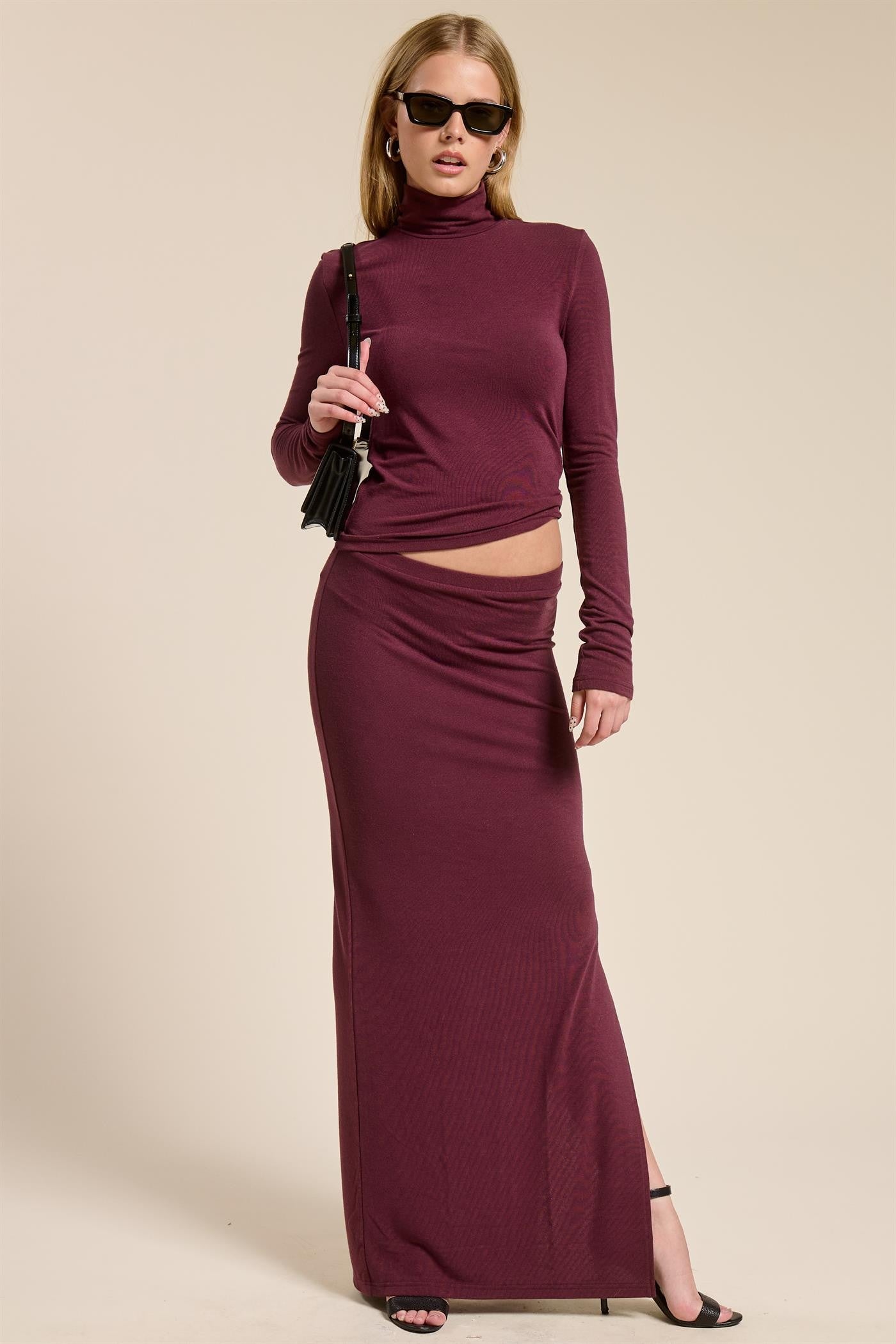 woman wearing a burgundy long sleeve crop top and matching maxi skirt, styled with sunglasses and a small bag