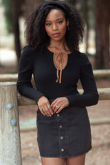 woman wearing a black ribbed long sleeve top with a tan neckline tie and a black denim mini skirt