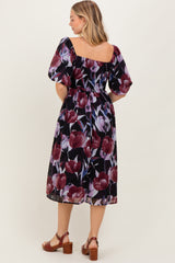 woman wearing a black floral mid-length dress with puff sleeves and a gathered waist, viewed from the back