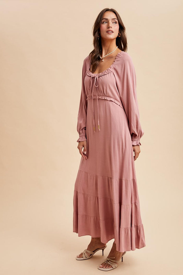 woman wearing a dusty rose long sleeve maxi dress with a drawstring neckline and tiered skirt
