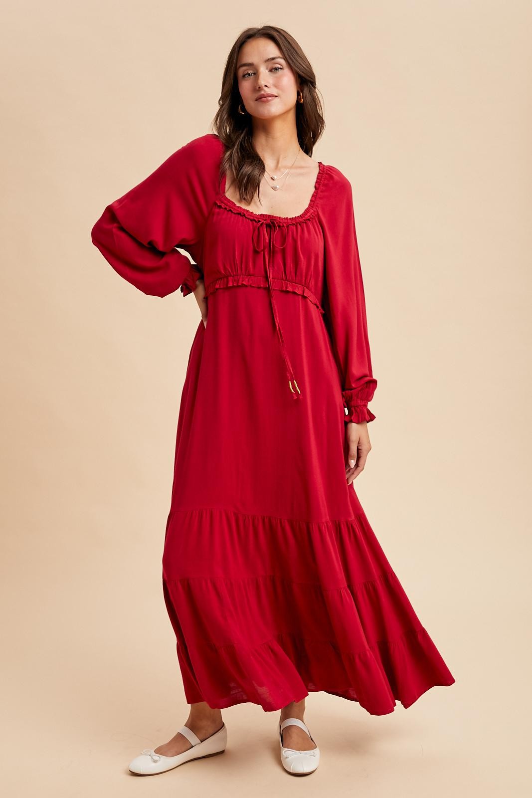 woman wearing a red long sleeve maxi dress with a cinched bodice and tiered skirt, styled with white flats