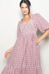 woman wearing a red and white checkered puff sleeve dress with a square neckline and tiered hem, posing with one hand in pocket