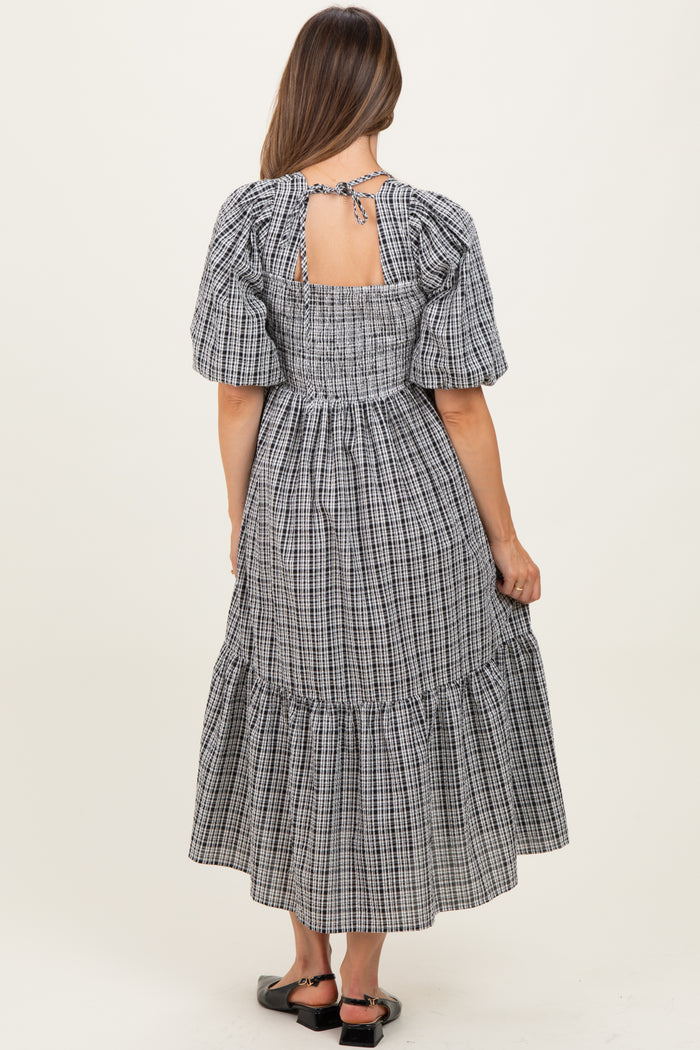 woman wearing a black and white checkered maternity dress with puff sleeves and a tie back detail