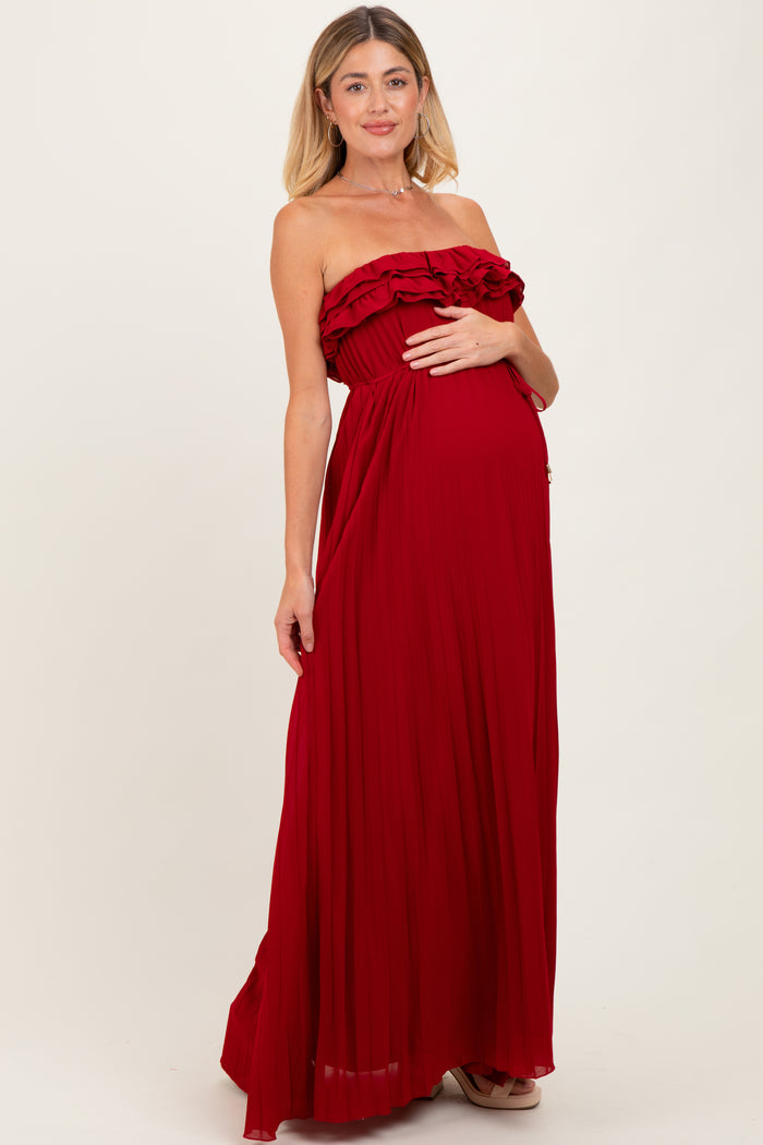woman wearing a red strapless maternity maxi dress with ruffle details, gently cradling her baby bump