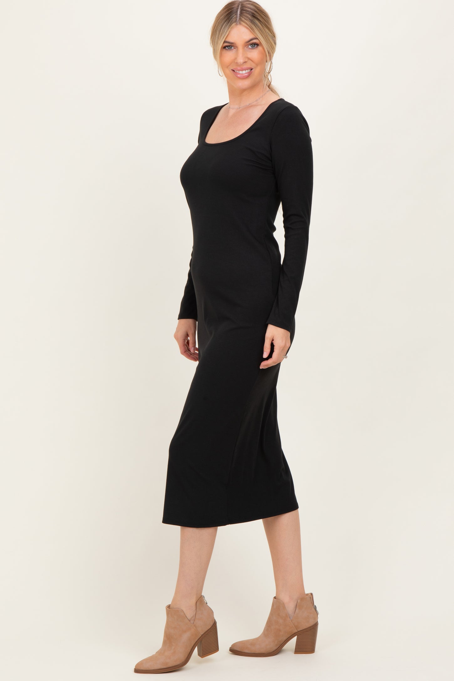 woman wearing a black long sleeve midi dress with a square neckline and styled with tan ankle boots